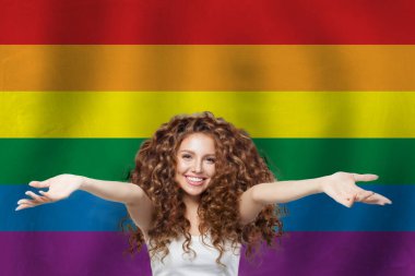 LGBT bayrağının arka planında kıvırcık saçlı mutlu kadın.