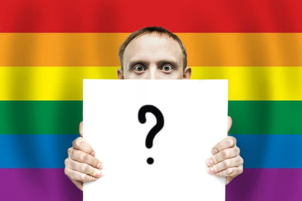 Surprised man holding white sign paper with question mark on the background o LGBT flag