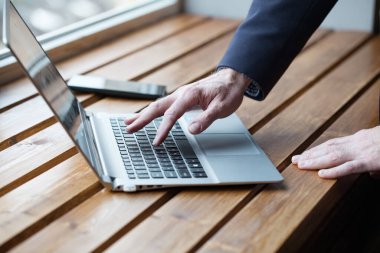 Bileğinde saati olan bir iş adamı dizüstü bilgisayarda çalışıyor, parmakları daktilo kullanıyor. Masayı kapat.