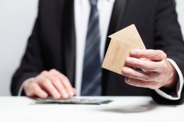 İşadamlarının elindeki ahşap ev ve biz dolar banknotları. Byuing mülkü, sigorta konsepti