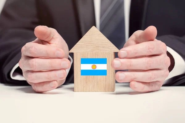 Businessman hand holding wooden home model with Argentine flag. insurance and property concepts