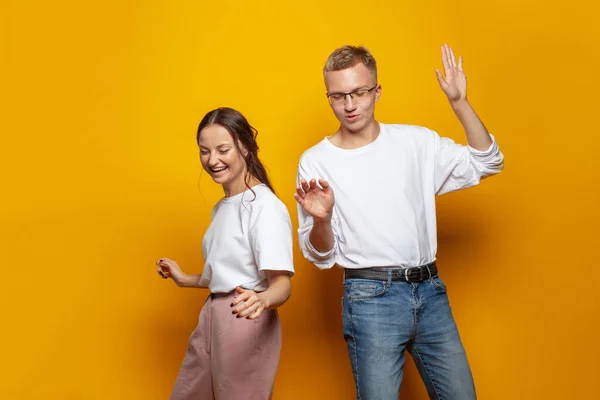 Cheerful couple man and woman dancing against colorful orange studio wall banner background