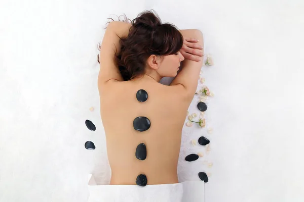 Beautiful brunette spa model woman with black stones on white background. Spa treatment and massage concept