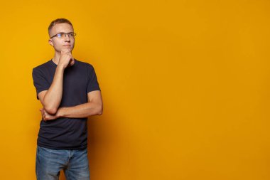 Gözlüklü genç adam sarı stüdyo duvarının arkasında tek başına durduğunu düşünüyor.