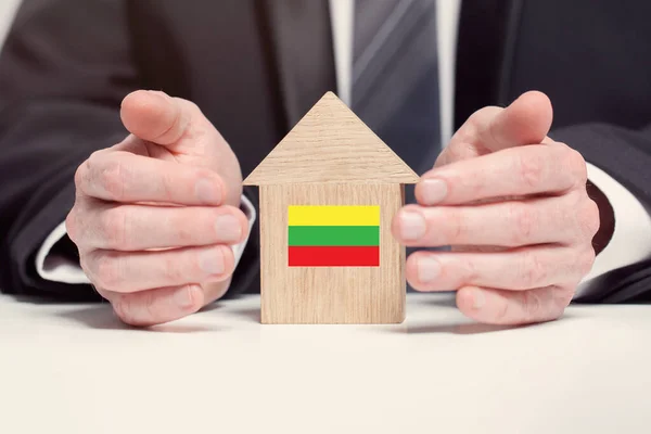 Businessman hand holding wooden home model with Lithuanian flag. insurance and property concepts