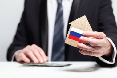 İş adamı elinde Rus bayrağıyla ahşap ev modelini tutuyor. sigorta ve mülkiyet kavramları