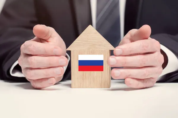 stock image Businessman hand holding wooden home model with Russian flag. insurance and property concepts