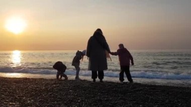 Anne ve çocuklar deniz kıyısında oynuyorlar. gün batımı ve mutlu insanlar.