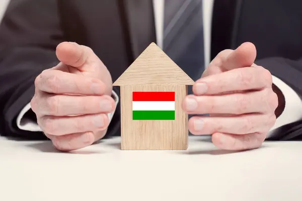 Businessman hand holding wooden home model with Hungarian flag. insurance and property concepts