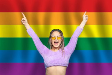 LGBT bayrağının arka planında elleri havada mutlu ve heyecanlı bir kadın hayrete düşmüş ya da şok olmuştu.