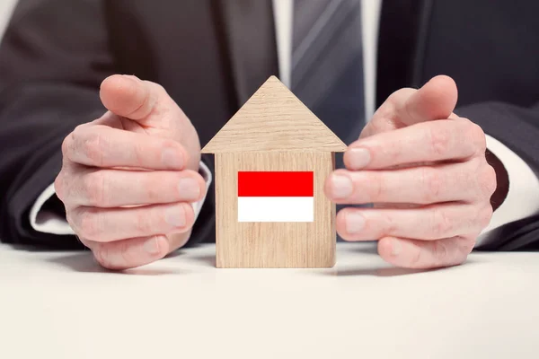 Businessman hand holding wooden home model with Monako flag. insurance and property concepts