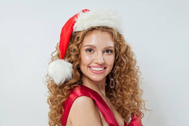 Noel Baba şapkalı genç mutlu kadın portresi. Uzun dalgalı saçları ve beyaz arka planda neşeli gülüşü olan güzel bir kadın manken.