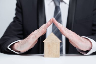 Takım elbiseli işadamının altında ahşap ev, sigorta güvenliği konsepti.