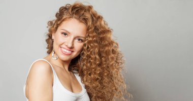 Kıvırcık, uzun, kahverengi saçlı, beyaz arka planda gülümseyen, sevimli, dost canlısı, çekici bir kadın. Dalgalı saçlı kadın