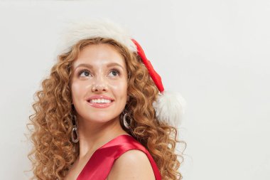 Noel Baba şapkası portresindeki güzel kızıl saçlı kadın. Uzun dalgalı saçları ve beyaz arka planda neşeli gülüşü olan güzel bir kadın manken.