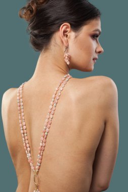 Moda bir mücevher modeli. Kolyesi ve küpesi mavi arka planda poz veren güzel bir kadın.