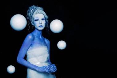 Mavi ve beyaz vücut sanatı, karnaval makyajı ve siyah arka planda beyaz uzay gezegeni küresi olan esrarengiz soğuk kadın.