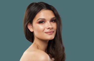 Güzel, genç, model, esmer, parlak, taze bir teni ve mavi arka planda uzun kıvırcık saçları olan bir kadın.