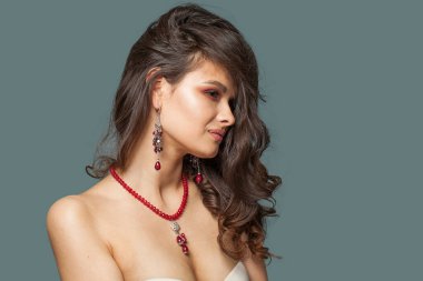 Yakışıklı, mücevher mankeni, esmer, sağlıklı, açık tenli, mavi arka planda koyu kahverengi saçlı bir kadın.