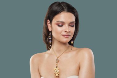 Sağlıklı, açık tenli, mavi arka planda koyu kahverengi saçlı, güzel bir mücevher modeli olan esmer kadın.