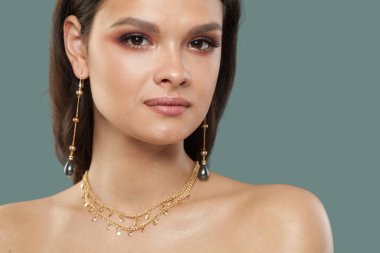 Mükemmel mücevher modeli esmer, sağlıklı, açık tenli, mavi arka planda koyu kahverengi saçlı kadın.