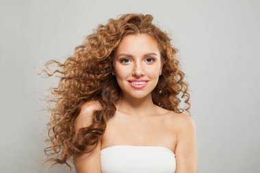 Güzel bir manken kadın, doğal makyajlı, açık tenli ve beyaz arka planda kıvırcık saçlı.