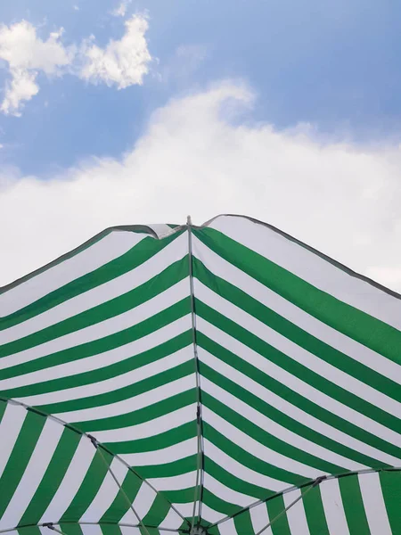 Green and white striped beach umbrella against sky with white cloud