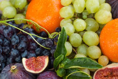 Renkli meyveler yakın plan. Üzüm, incir, yeşil yapraklı turuncu mandalina ve çiğ suyu.