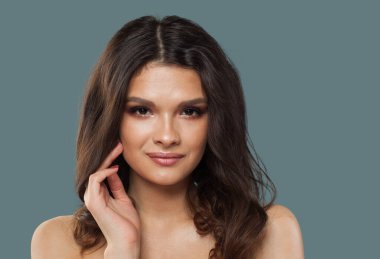 Parlak, taze bir teni ve mavi arka planda uzun kıvırcık saçları olan güzel, genç model esmer kadın.