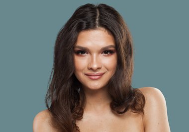 Gülümseyen genç model esmer kadın. Parlak, taze tenli ve mavi arka planda uzun kıvırcık saçlı.