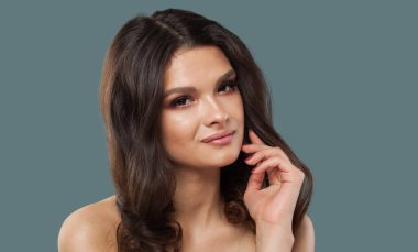 Sağlıklı, genç model esmer, parlak, taze bir teni ve mavi arka planda uzun kıvırcık saçları olan kadın.