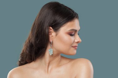 Mücevher küpeli muhteşem esmer kadın mavi arka planda poz veriyor.