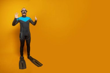Scuba diver man showing six fingers up on yellow studio wall background clipart
