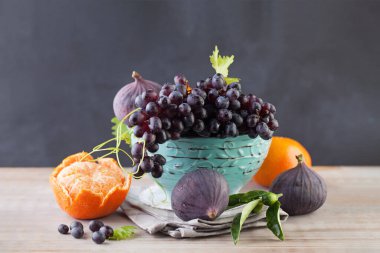 Üzüm, mandalina ve incir meyvesi mavi kasede, ahşap masada, sağlıklı yemek arka planında. Diyet, früktoz ve vitamin konsepti