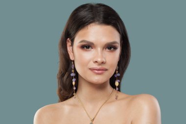 Şirin, genç, esmer, mücevher modeli portresi. Uzun kahverengi saçlı, doğal makyajlı, temiz tenli, stüdyo portresi olan bir kadın.