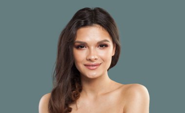 Güzel, genç model esmer, parlak, taze tenli ve mavi arka planda uzun kıvırcık saçlı bir kadın.