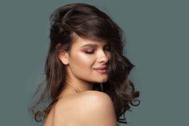 Dalgalı koyu kahverengi saç stili ve mavi stüdyo arka planında taze parlak cildi olan genç model kadın, moda portresi. Cilt bakımı, saç bakımı ve kozmetik konsepti