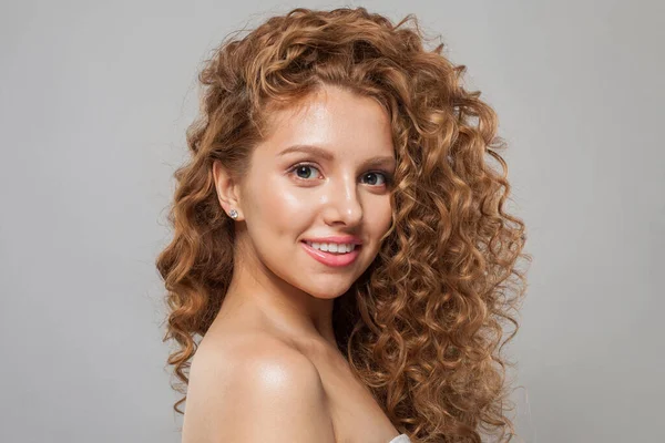 Cheerful young female model healthy woman with long wavy frizzy hairstyle and clear skin studio portrait. Hair care, facial treatment and cosmetology concept