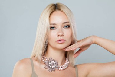 Sarışın, manken, açık tenli, uzun sarı saçlı, takı inci kolyeli, gri stüdyo arka planında poz veren, moda güzeli portresi olan bir kadın.