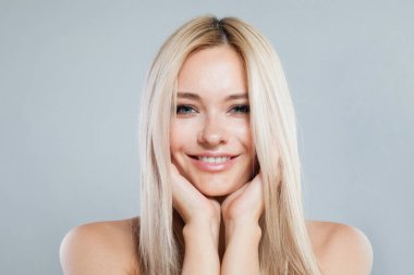 Çekici, güler yüzlü, güzel saçlı, mutlu bir kadın model. Saf parlak tenli ve gri arka planda sarı saçlı güzel bir kadının stüdyo fotoğrafı.