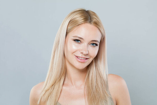 Nice smiling joyfully female model with fair hair looking at camera, being happy. Studio shot of good-looking beautiful woman with pure shiny skin and blonde hair on gray background