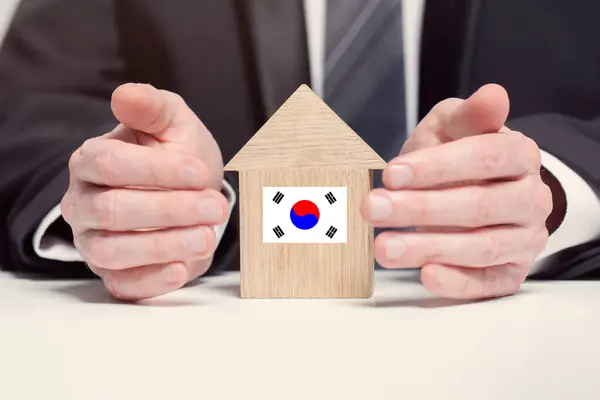 Businessman hand holding wooden home model with Korean flag. insurance and property concepts