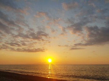 Turuncu ve altın rengi günbatımı bulutlu ve okyanus plajlı gökyüzü