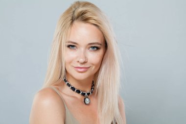 Temiz, taze, sarı saçlı, siyah takı kolyesi takan, gri stüdyo arka planında poz veren neşeli manken kadın. Moda güzellik portresi.