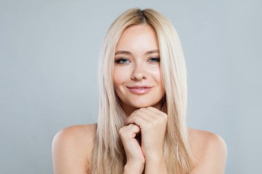 Güzel gülümseyen, neşeli, sarışın, kameraya bakan, mutlu bir kadın model. Saf parlak tenli ve gri arka planda sarı saçlı güzel bir kadının stüdyo fotoğrafı.