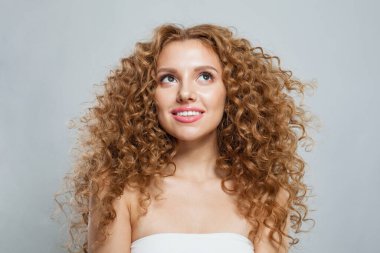 Kızıl saçlı, uzun kıvırcık saçlı ve beyaz arka planda poz veren güzel bir kadın model. Stüdyo moda güzellik portresi