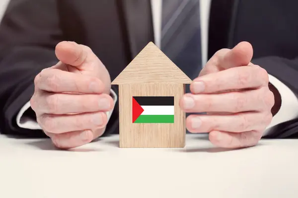 Businessman hand holding wooden home model with Palestinian flag. insurance and property concepts