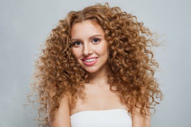 Kızıl saçlı, uzun kıvırcık saçlı ve beyaz arka planda poz veren temiz, taze tenli neşeli bir manken. Stüdyo moda güzellik portresi