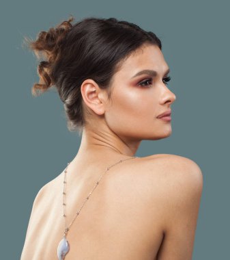 Makyajlı, şık, esmer, güzel bir manken, dalgalı saç stili ve mavi arka planda poz veren sağlıklı bir ten. Kolyeli bir kadının portresi.