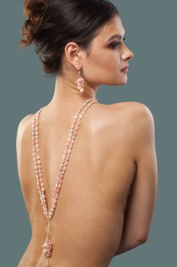 Makyajlı, dalgalı saç stili ve mavi arka planda poz veren güzel, esmer bir manken. Kolyeli bir kadının portresi.